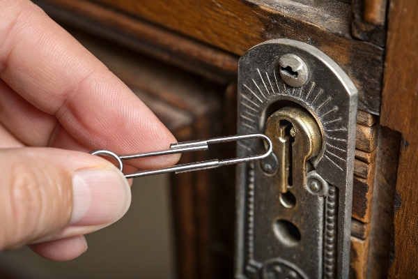 Person using a paperclip to pick a vintage lock, showcasing a DIY approach to lock unlocking