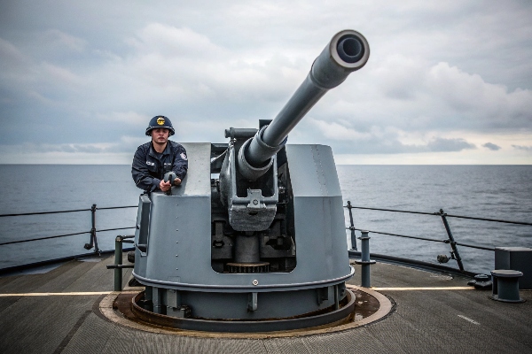 Naval officer standing by a large deck-mounted gun on a warship.