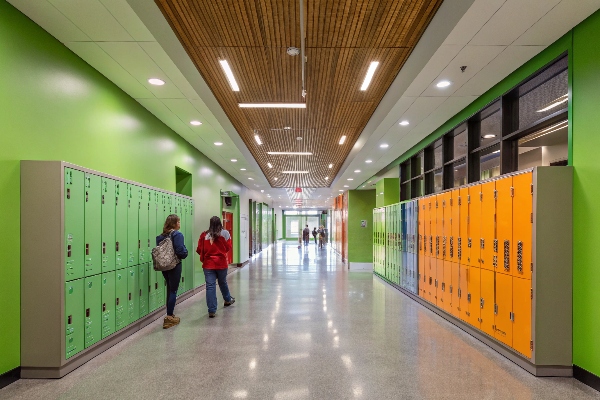 Green and orange lockers in a brightly lit school hallway with a wooden ceiling.