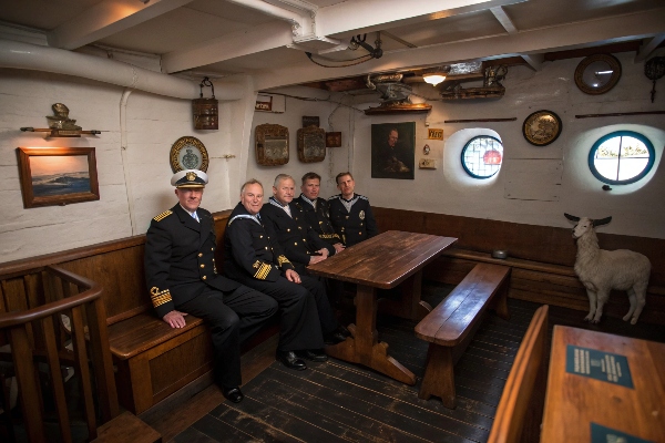 Naval officers sitting together inside a historic ship's cabin.