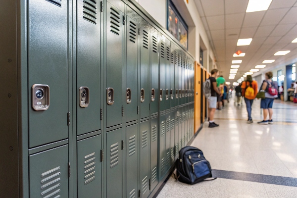 Dark green lockers in a school hallway with students and a backpack on the floor.