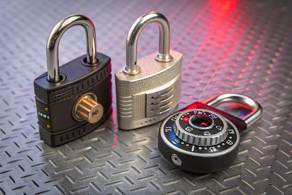 Three types of padlocks placed on a metal surface: smart lock, combination lock, and traditional lock.