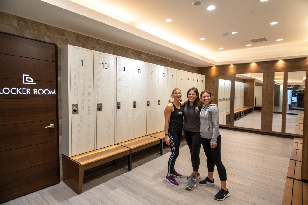 Luxury gym locker room with white lockers and three smiling women